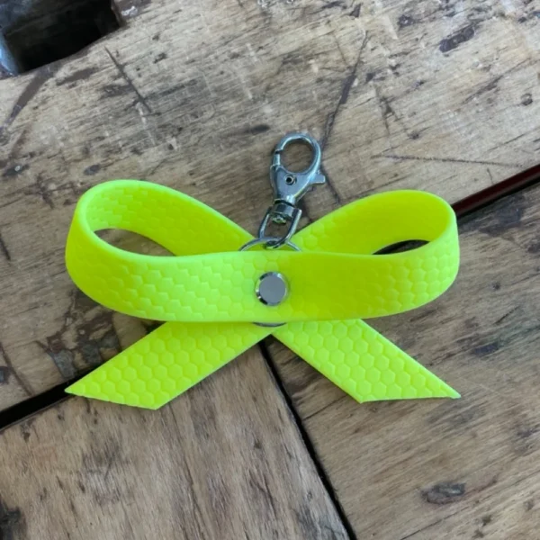 Eine gelbe Schleife aus dem Material Hexa mit Karabiner, damit man die Schleife an dem Halsband seines Hundes befestigen kann. Eine gelbe Schleife oder ein gelbes Halstuch sollen kennzeichnen, dass entsprechende Hunde mehr Abstand brauchen.