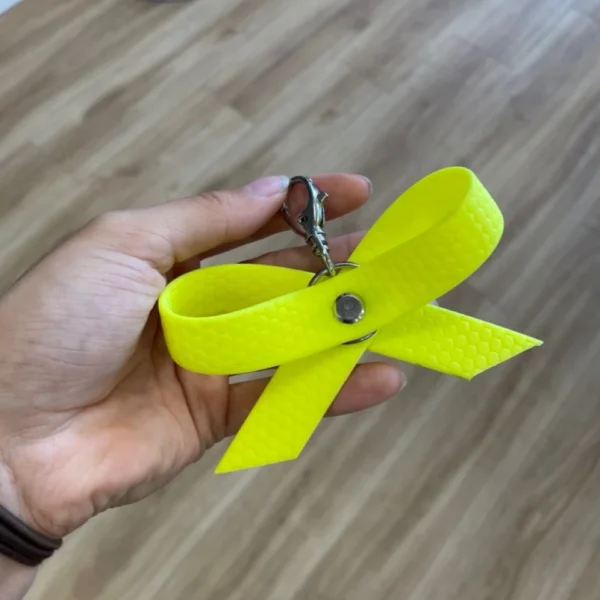 Eine gelbe Schleife aus dem Material Hexa mit Karabiner, damit man die Schleife an dem Halsband seines Hundes befestigen kann. Eine gelbe Schleife oder ein gelbes Halstuch sollen kennzeichnen, dass entsprechende Hunde mehr Abstand brauchen.