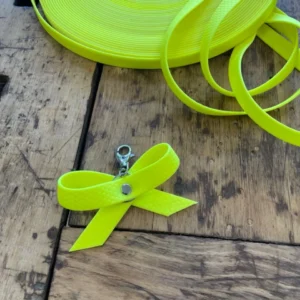 Eine gelbe Schleife aus dem Material Hexa mit Karabiner, damit man die Schleife an dem Halsband seines Hundes befestigen kann. Eine gelbe Schleife oder ein gelbes Halstuch sollen kennzeichnen, dass entsprechende Hunde mehr Abstand brauchen.